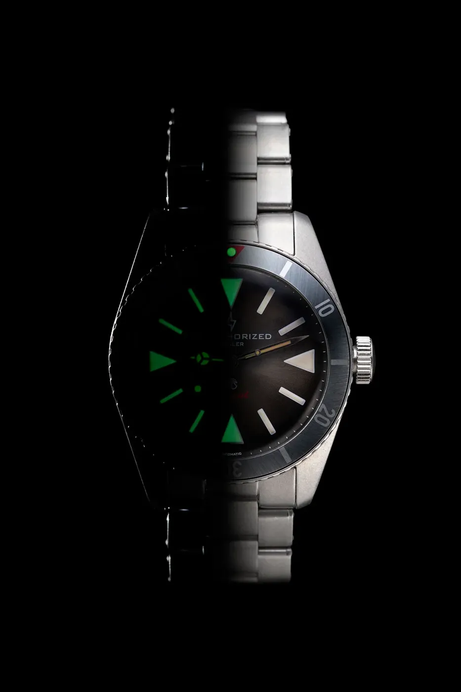 Montre en acier photographiée sur fond noir, index lumineux