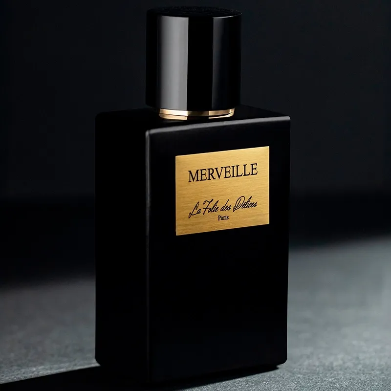 Flacon de parfum noir à étiquette dorée photographié en lumière rasante